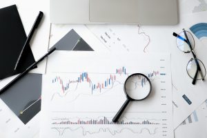 pexels-photo-6801648-6801648 Flat lay of stock market analysis documents with magnifying glass, pens, and glasses.
